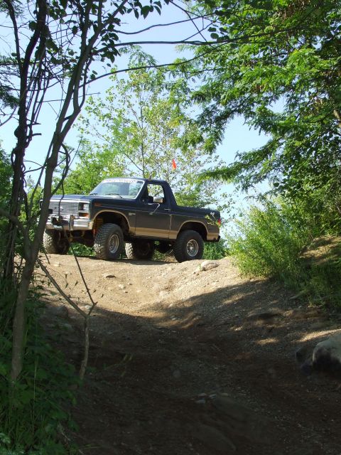 1986 Ford Bronco - A black Ford Bronco navigates an off-road trail, its lifted suspension and large tires evident.