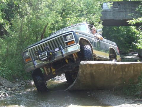 1986 Ford Bronco - 1986 Ford Bronco navigating a challenging off-road course with water and concrete obstacles.