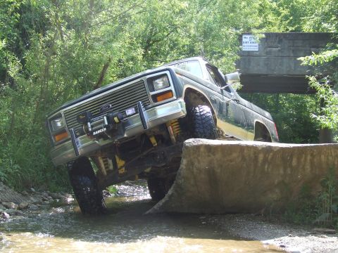 1986 Ford Bronco - This truck is navigating a challenging off-road course, with one wheel lifted high.