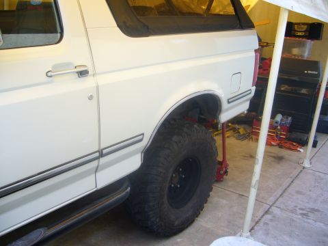 1992 Ford Bronco - The rear quarter panel and large off-road tires of a white 1992 Ford Bronco are visible.