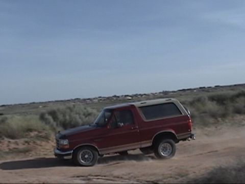 1994 Ford Bronco - This SUV is kicking up dust as it drives along a dry, barren landscape under a clear sky.