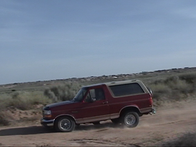 Red Ford Bronco with a tan top driving on a dirt road, kicking up dust