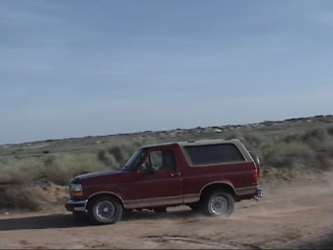 1994 Ford Bronco - This 1994 Ford Bronco kicks up dust as it drives along a dirt road under a clear blue sky.