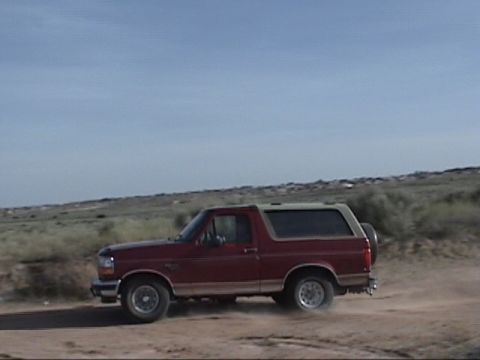 1994 Ford Bronco - 1994 Ford Bronco driving on a dirt road in a dry, open landscape.