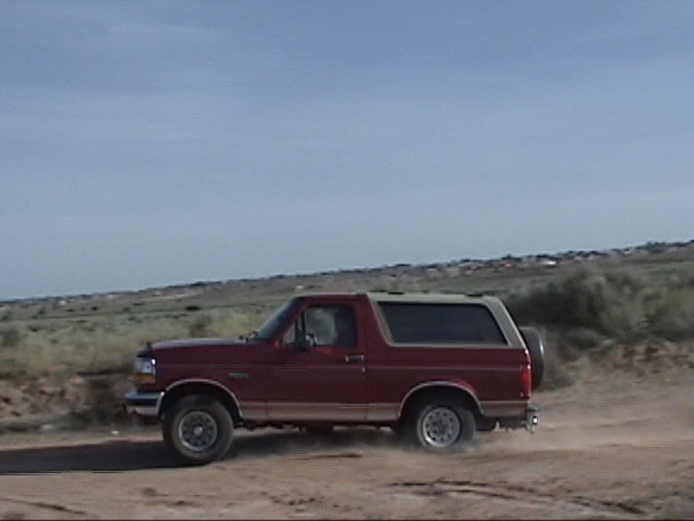 Red 1994 Ford Bronco driving on a dirt road with a spare tire on the back