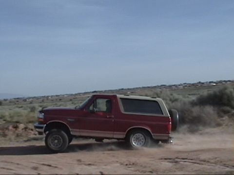 1994 Ford Bronco - Red 1994 Ford Bronco driving on a dusty dirt road in a dry, open landscape.