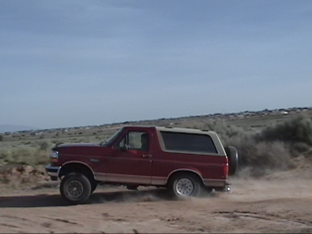 1994 Ford Bronco driving on a dirt road, kicking up dust. Side view