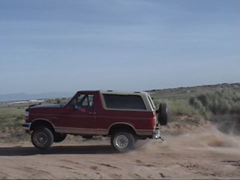 1994 Ford Bronco - Red 1994 Ford Bronco driving on a dirt road with a spare tire on the back.