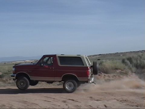 1994 Ford Bronco - This SUV is kicking up dust as it drives on a dirt road with a spare tire on the back.