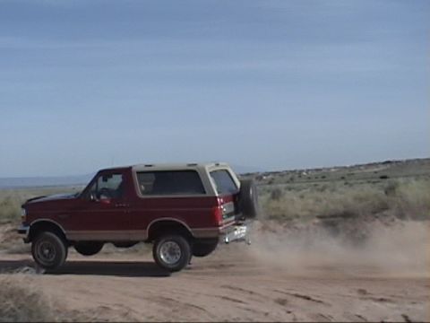 1994 Ford Bronco - 1994 Ford Bronco driving on a dirt road, kicking up dust. Spare tire mounted on rear.
