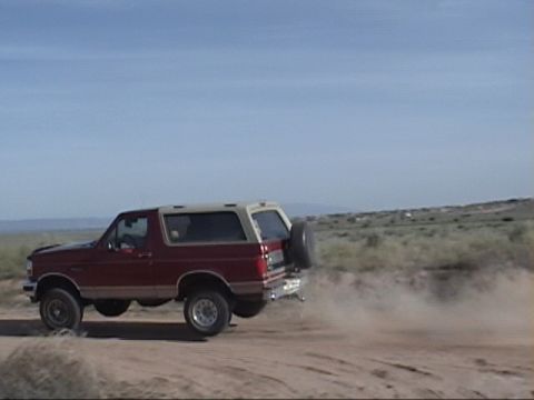 1994 Ford Bronco - This Ford Bronco is captured mid-air on a dusty road, its body style suggesting a model year in the early to mid-1990s.
