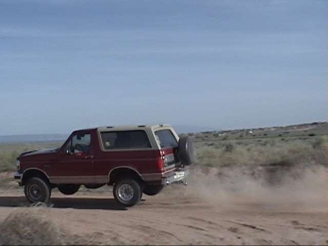 Red and tan Ford Bronco with a spare tire on the back, kicking up dust on a dirt road