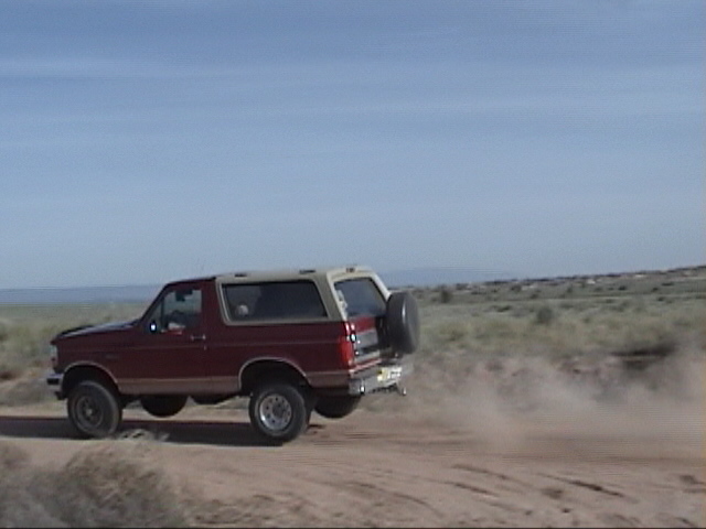 Red and tan 1994 Ford Bronco side view, kicking up dust