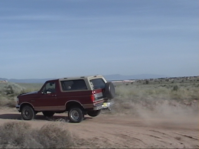 Red and tan SUV kicking up dust on a dirt road, spare tire mounted on the rear