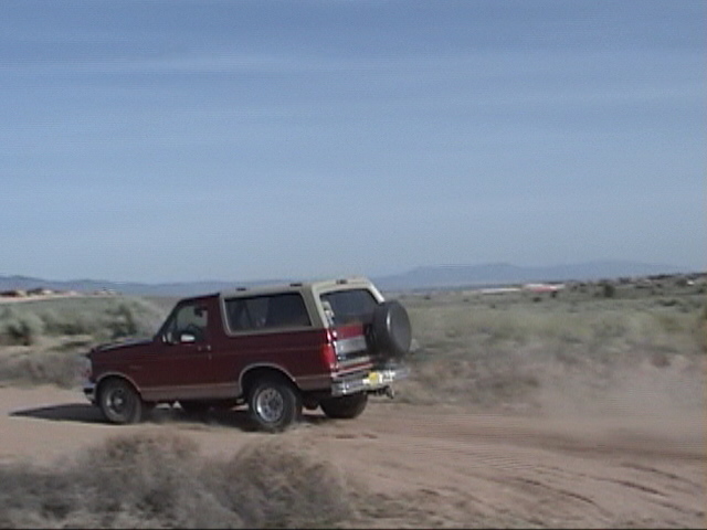 1994 Ford Bronco driving on a dirt road in a dry, open landscape