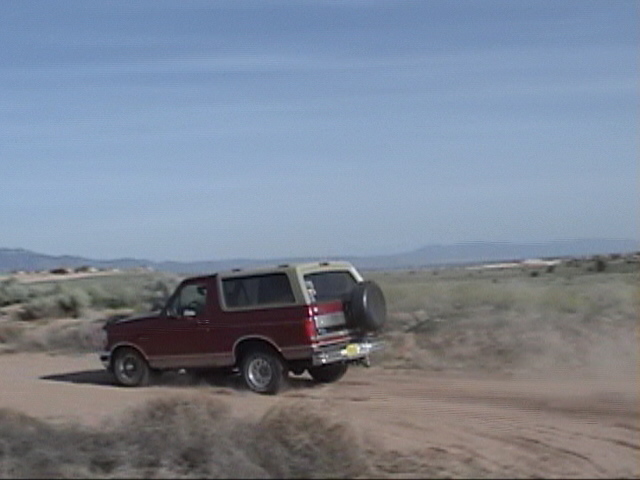 red SUV with spare tire on back driving on a dirt road in a dry, open landscape