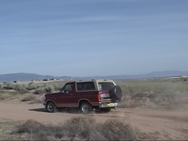 1994 Ford Bronco rear view, red and tan, driving on dirt road