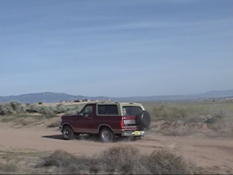 1994 Ford Bronco - A Ford Bronco drives down a dusty road under a clear blue sky.