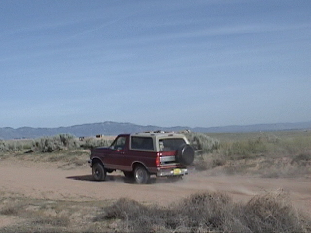 Red and tan Ford Bronco driving on a dirt road with mountains in the background