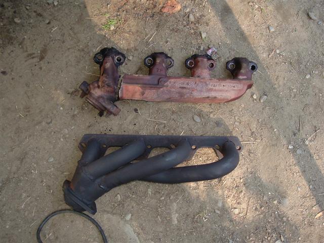 Two exhaust manifolds on the ground, one rusty and one black
