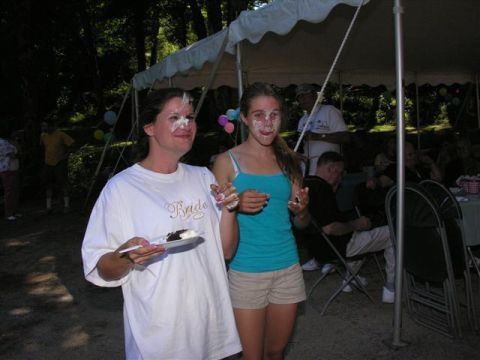 1966 Land Rover Discovery - Two women, one wearing a 'Bride' shirt, have pie smeared on their faces during an outdoor celebration.