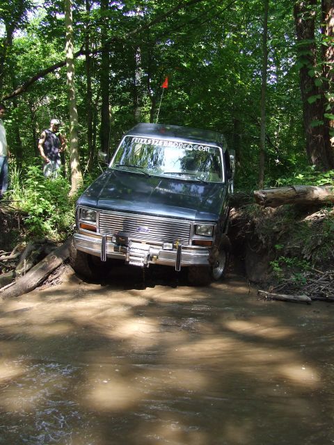 1986 Ford Bronco - This 1986 Ford Bronco is navigating a challenging off-road trail through water and trees.