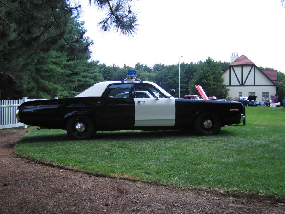 Black and white vintage police sedan in profile parked on grass at a car show
