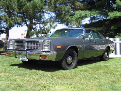 1991 Ford LTD Crown Victoria - Front three-quarter view of a gray 1970s full-size four-door sedan with stacked headlights, parked on grass near a white fence.