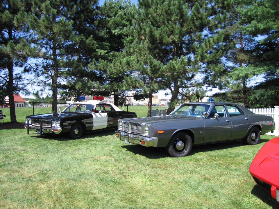 black-and-white police sedan parked beside a gray sedan on grass at a show