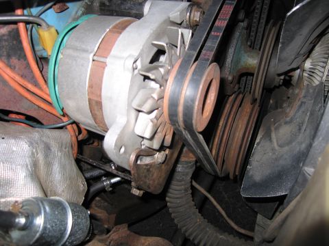 1991 Ford LTD Crown Victoria - Close-up of an alternator driven by a V-belt with pulleys, surrounded by hoses and grime inside an engine bay.