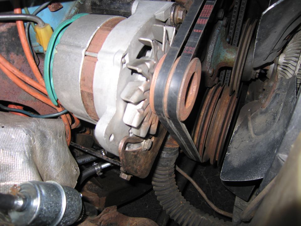 Close-up of an alternator and V-belt pulleys inside a dirty engine bay