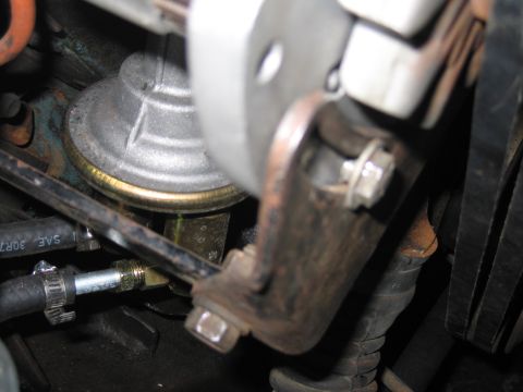 1991 Ford LTD Crown Victoria - Close-up of an engine pulley and mounting bracket with bolts and a hose clamp inside a greasy engine bay.