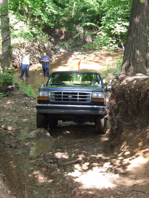 1986 Ford Bronco - This Ford truck is driving through a muddy, wooded area with two people watching.