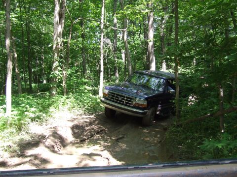 1986 Ford Bronco - Ford Bronco navigating a muddy off-road path surrounded by dense trees.