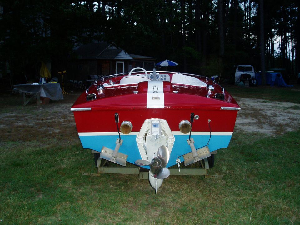 Red and blue boat on trailer, rear view. Outdrives and propeller visible
