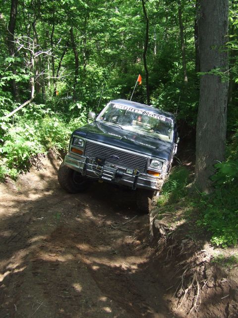 1986 Ford Bronco - Ford Bronco tackling an off-road trail with steep inclines and muddy terrain.