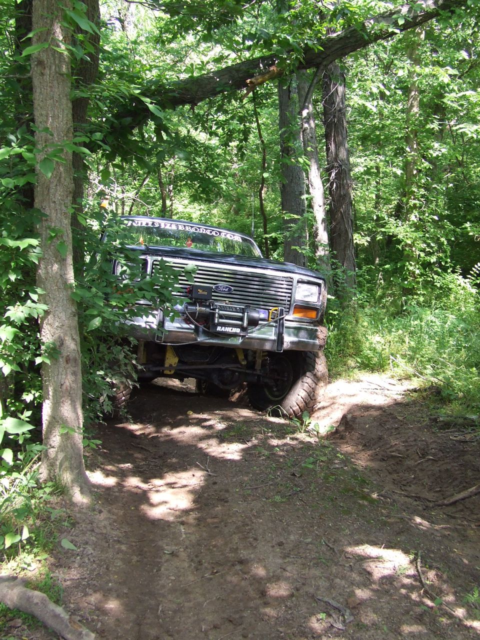Ford Bronco on a dirt trail in the woods, front end angled towards the camera