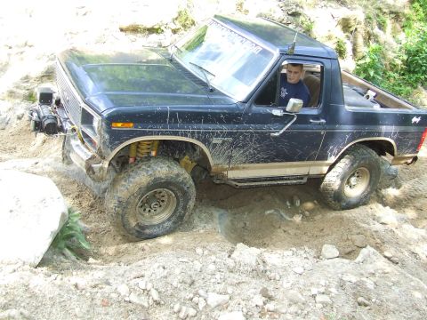 1986 Ford Bronco - This off-road SUV, likely from the early 1980s, navigates a challenging dirt terrain.