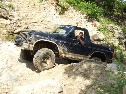 1986 Ford Bronco - A man drives a dark-colored Ford Bronco through a challenging off-road course.