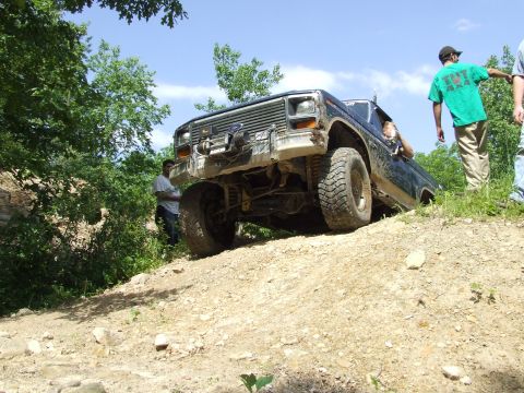 1986 Ford Bronco - A dark blue Ford Bronco navigates a steep dirt incline during an off-road excursion.