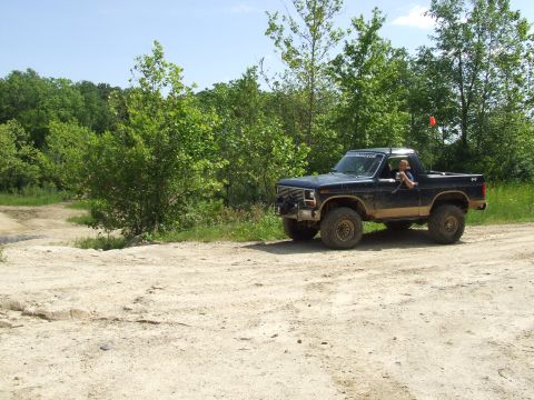 1986 Ford Bronco - This modified pickup truck, likely from the early 1980s, navigates a dirt track surrounded by trees.