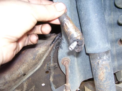 1996 Ford Bronco - A hand holds a frayed brake line, revealing damage to the vehicle's undercarriage.
