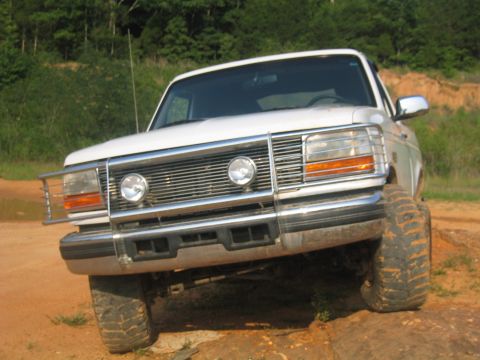 1996 Ford Bronco - This white Ford Bronco, likely from the early to mid-1990s, is shown from the front on an uneven dirt surface.