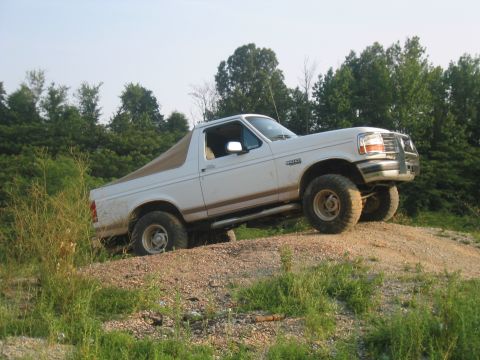 1996 Ford Bronco - White 1996 Ford Bronco navigates an off-road incline with a tan soft top.