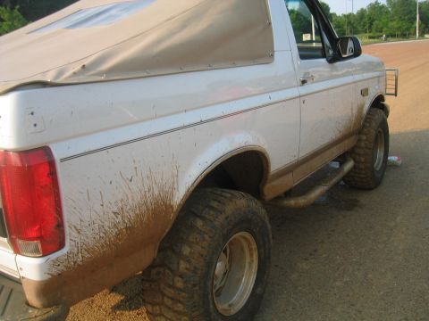 1996 Ford Bronco - This mud-splattered Ford Bronco is shown from the rear three-quarter angle, highlighting its off-road capabilities.