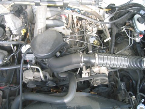 1996 Ford Bronco - Overhead view of a Ford EFI V8 engine bay with the ribbed cast intake plenum marked 5.8L, a black plastic air box feeding a corrugated inta…