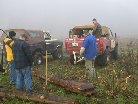 1978 Ford Bronco - Two 1978 Ford Broncos are present while people work with logs in a foggy outdoor scene.
