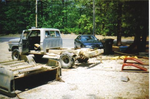 1979 Ford F-250 - A disassembled Ford truck sits in a yard next to a dark sedan and some discarded parts.