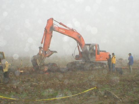 1978 Ford Bronco - An orange excavator is actively digging in a muddy, outdoor scene, with a yellow jeep visible to the left.