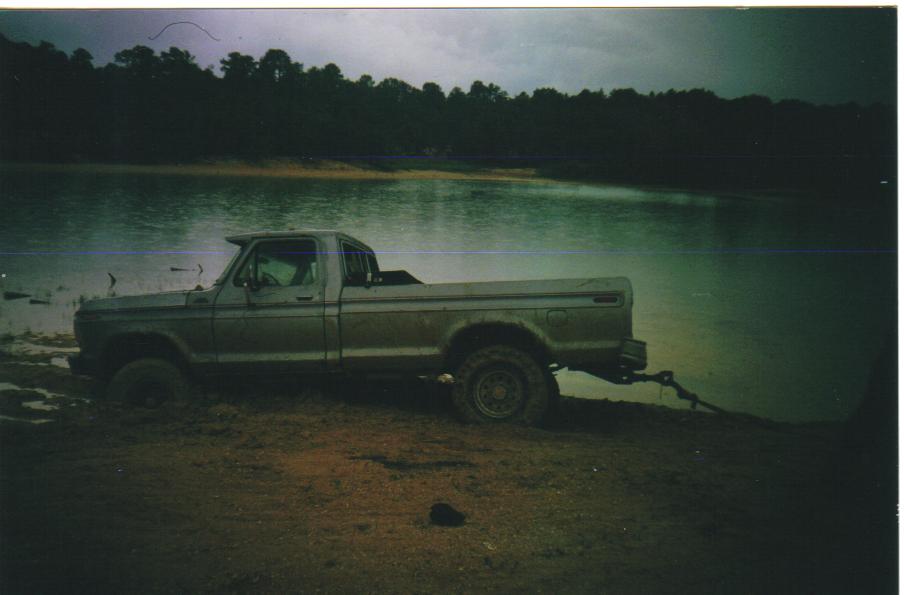 1979 Ford F-250 stuck in mud next to a lake, being pulled by a chain